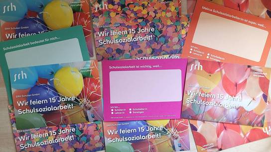Zahlreiche farbefrohe Postkarten zum 15-jährigen Jubiläum der Schulsozialarbeit der SRH Schulen Jugendhilfe liegen neben- und übereinander.