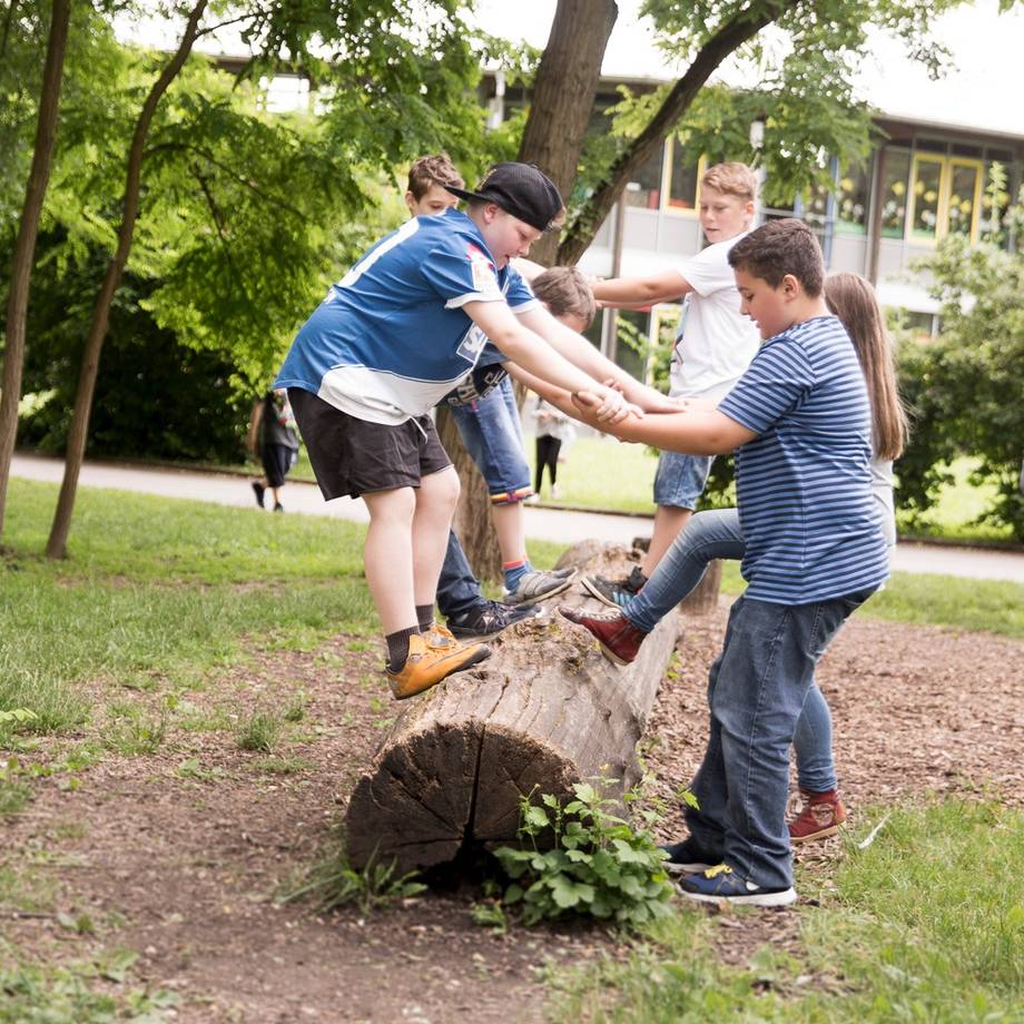 Jugendliche balancieren auf einem Baumstamm und geben sich gegenseitig Halt.